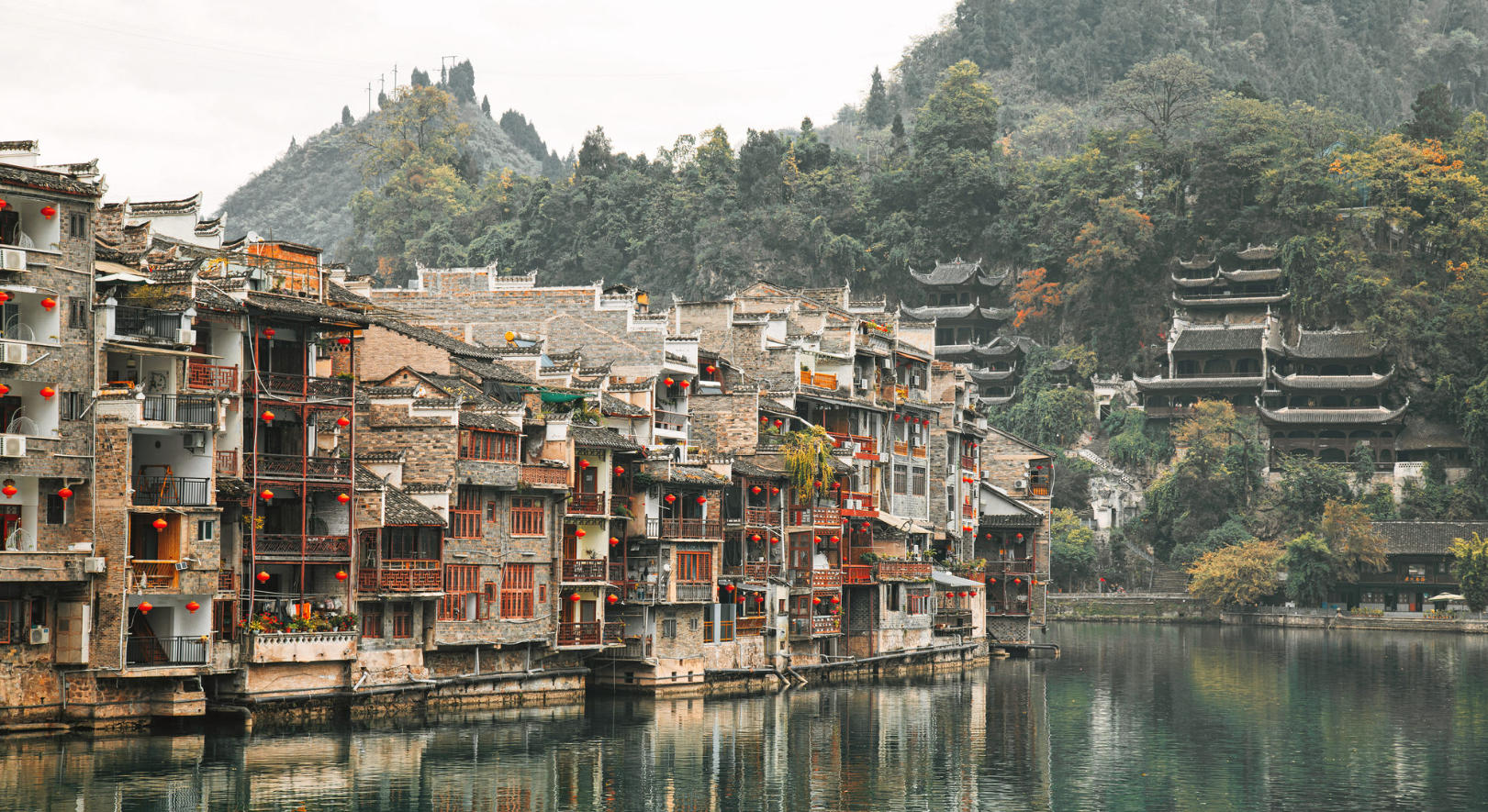 Traditional riverside buildings along the Wuyang River in Zhenyuan Ancient Town, framed by green hills.