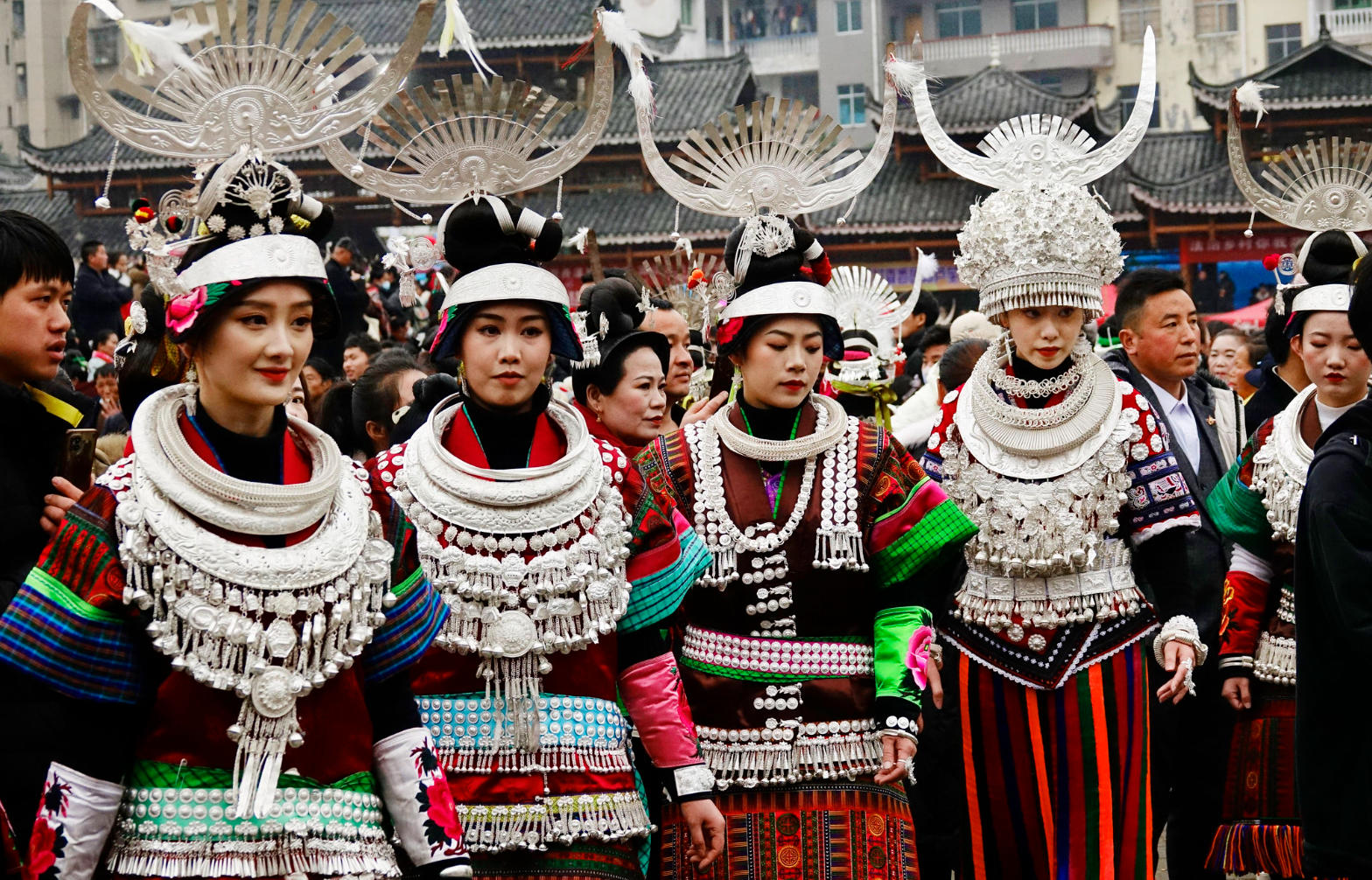  Miao women wearing elaborate traditional dress with silver headpieces and embroidered skirts, prepared for a festival celebration.

