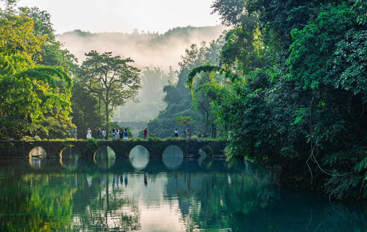 The seven-arched stone bridge at Xiaoqikong in Libo, set over turquoise water and surrounded by lush karst forest.