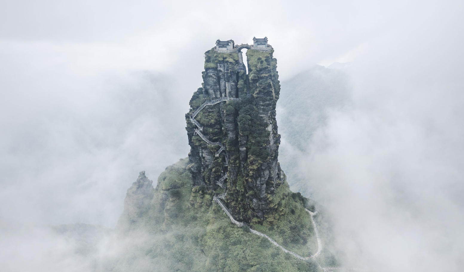 Misty peaks and rock formations of Mount Fanjing rising above a sea of clouds, with forested slopes below.